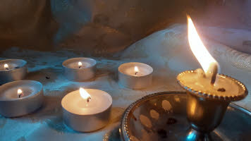 A picture of a nearly burnt out candle in a saucered candle holder with lighted tea lights in the background.