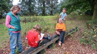 Forest Church participants using a low-level cross country horse jump made of car tyres as a convenient bench.